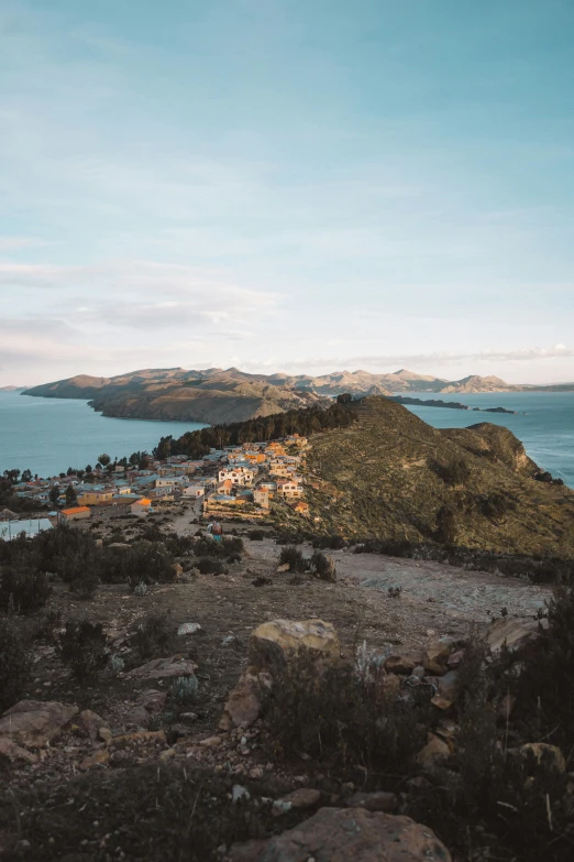 a person standing on top of a hill next to a body of water, quechua, aerial view of a city, taken at golden hour, an island