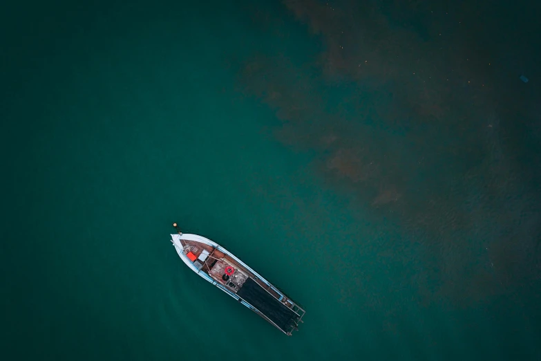 a small boat floating on top of a body of water, by Sebastian Spreng, pexels contest winner, top - down, dark green water, thumbnail, carson ellis
