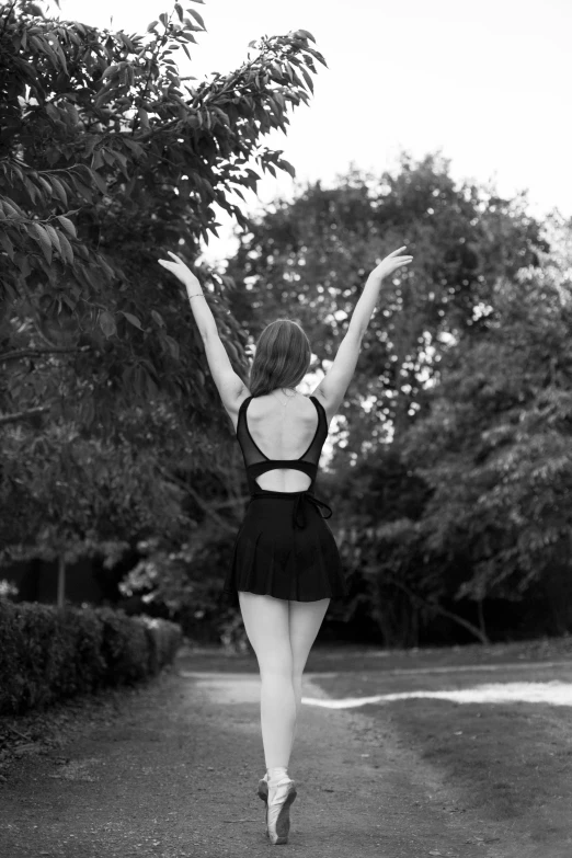 a black and white photo of a ballerina jumping in the air, inspired by Diane Arbus, tumblr, open back dress, walking at the garden, in retro swimsuit, standing with her back to us