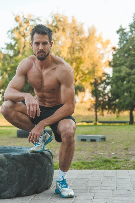 a man squatting on a tire in a park, mid-shot of a hunky, #trending, square masculine jaw, steroids