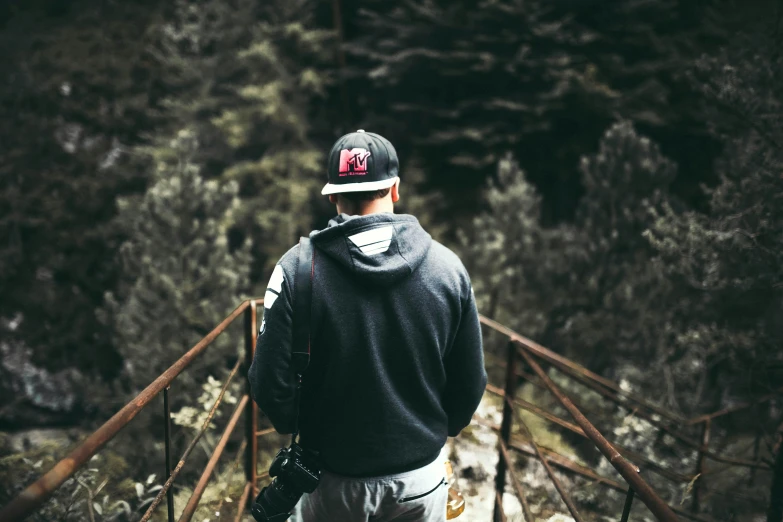 a man standing on top of a wooden bridge, pexels contest winner, wearing a backwards baseball cap, gray hoodie, standing in a grotto, seen from the back
