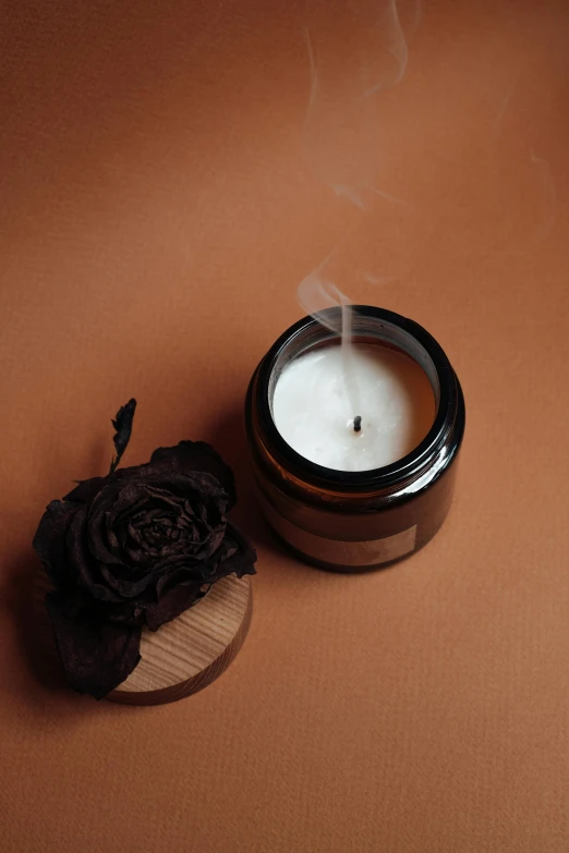 a candle sitting on top of a table next to a flower, detailed product image, thick pigmented smoke, brunette, dark. no text