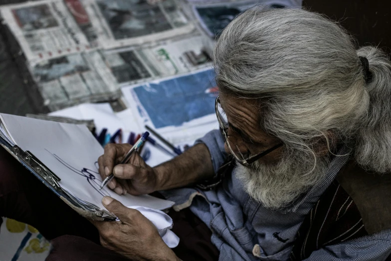 a man sitting on the ground writing on a piece of paper, a drawing, pexels contest winner, bengal school of art, old gigachad with grey beard, painting on a canvas, newspaper photography, disney artist