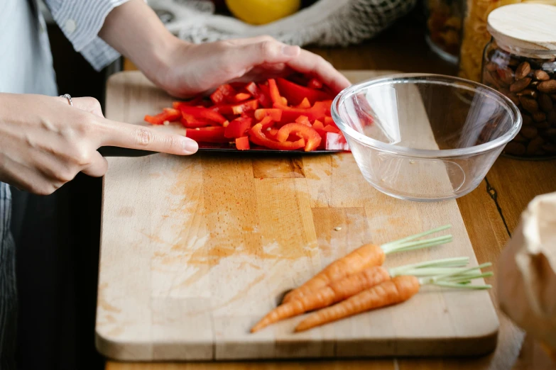 a person cutting up some red peppers on a cutting board, by Julia Pishtar, carrot, thumbnail, tabletop, plastic wrap