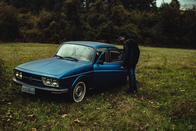 a man standing next to a blue car in a field, an album cover, by Elsa Bleda, pexels contest winner, renault ultimo, outside on the ground, fall season, profile picture