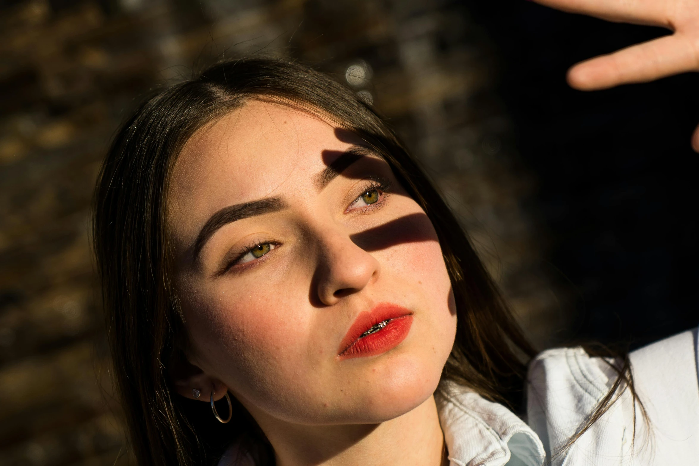 a woman standing in front of a brick wall, inspired by Elsa Bleda, pexels contest winner, photorealism, red lipstick on face, directional sunlight skewed shot, maisie williams, during an eclipse