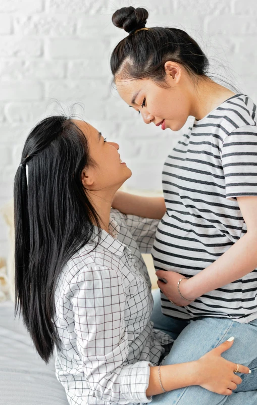 a woman sitting on top of a bed next to a woman, inspired by Ruth Jên, trending on pexels, pregnant belly, asian male, facing each other, promotional photo