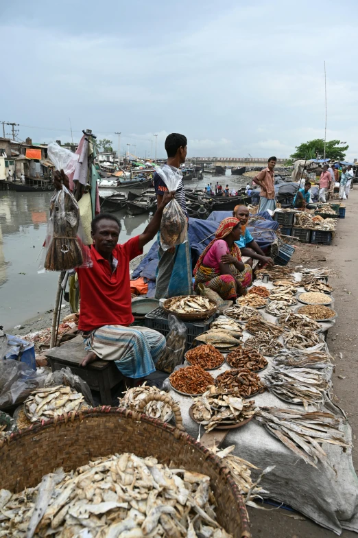 a group of people sitting next to a body of water, a picture, busy market, bangladesh, slide show, fishes
