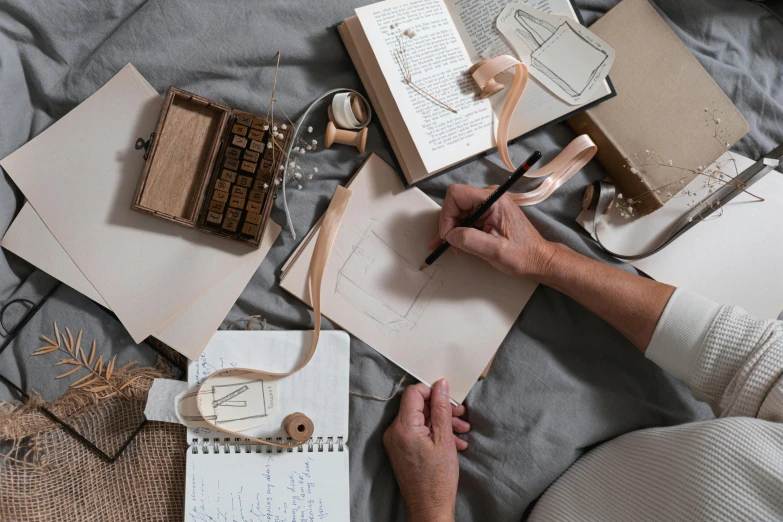 a woman sitting on a bed writing on a piece of paper, a drawing, by Sylvia Wishart, trending on pexels, knolling, delicate embellishments, cardboard, pyrography