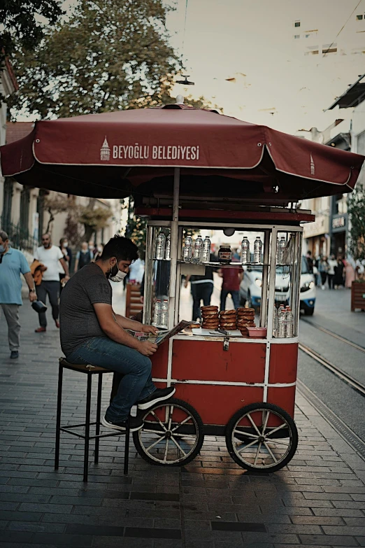 a man sitting at a food cart on a city street, pexels contest winner, fallout style istanbul, paul barson, tripod, brown