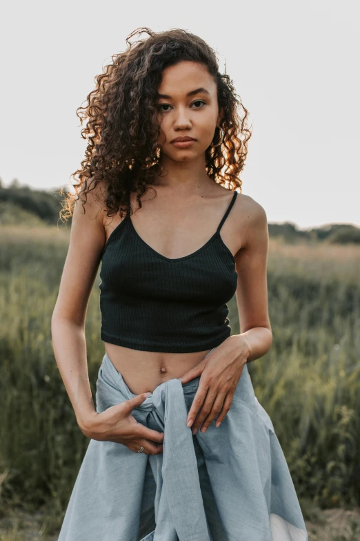 a woman standing in the middle of a field, trending on pexels, wearing a black cropped tank top, with textured hair and skin, revealing clothes, modern casual clothing