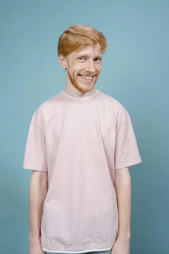 a man standing in front of a blue background, featured on reddit, pink clothes, ginger hair, on a pale background, ((pink))