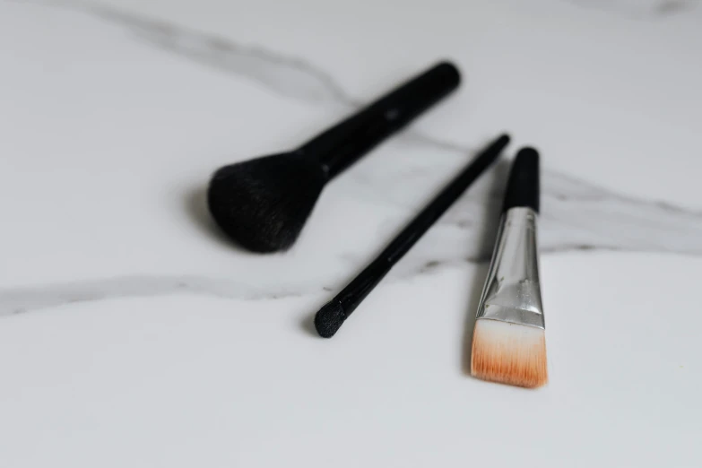 a couple of brushes sitting on top of a counter, a stipple, by Robbie Trevino, unsplash, photorealism, relaxed eyebrows, on a pale background, marble white complexion, black eyeliner