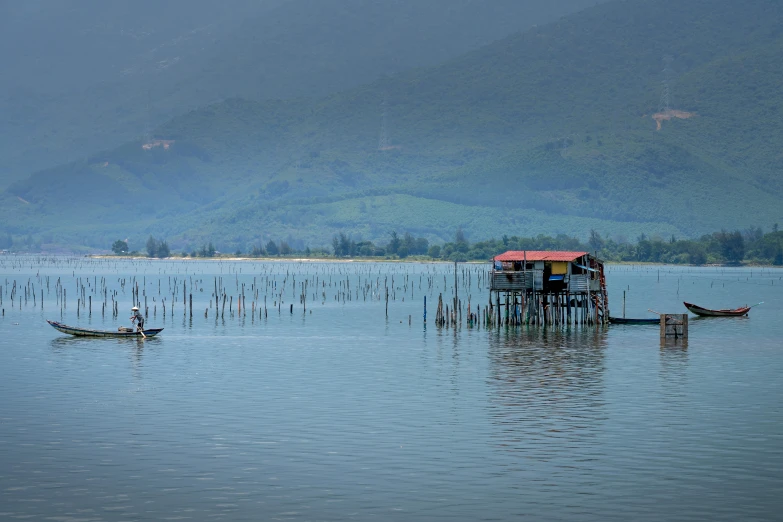 a person on a small boat in a large body of water, by Matteo Pérez, hurufiyya, bamboo huts, lake blue, on stilts, distant photo