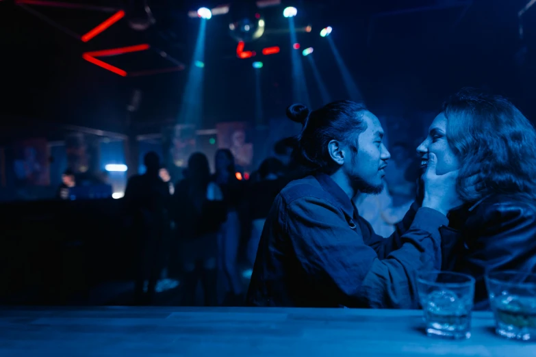 a couple of women sitting next to each other at a table, inspired by Nan Goldin, unsplash, happening, nightclub, asian man, blue, reylo kissing