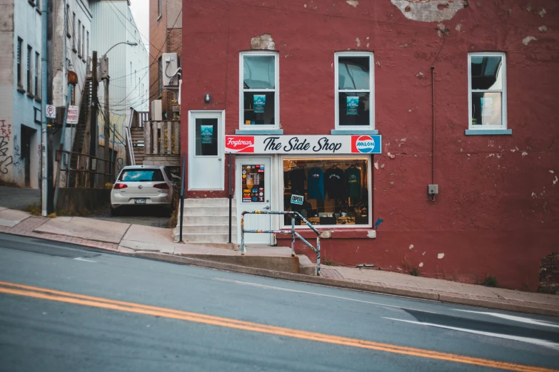 a red building sitting on the side of a road, a photo, the store, slate, streetwear, built on a steep hill