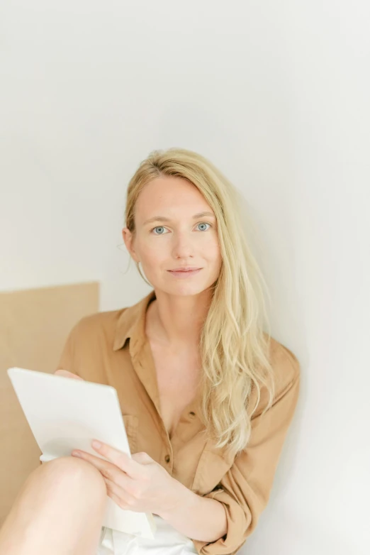 a woman sitting on a bed reading a book, by Sara Saftleven, shoulder - length blonde hair, on a white table, looking serious, on white paper