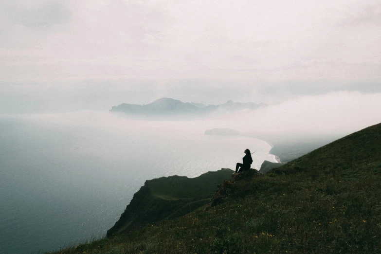 a person sitting on a hill overlooking a body of water, by Emma Andijewska, pexels contest winner, slight fog, skye meaker, views to the ocean, tiny person watching