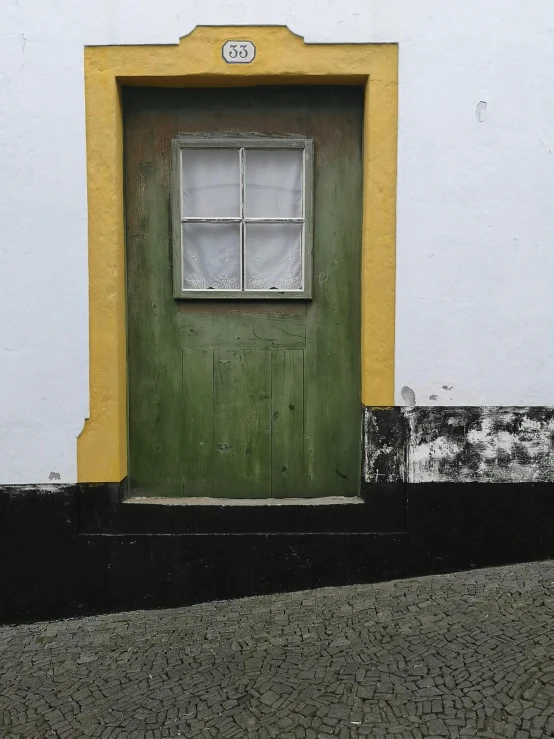 a green door sitting on the side of a white building, an album cover, by Alejandro Obregón, pexels contest winner, quaint village, buildings covered in black tar, vibrant but dreary gold, grey