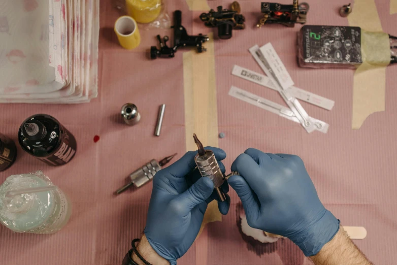 a person in blue gloves holding a pair of scissors, a tattoo, coating a stubborn core.', bird's eye, small vials and pouches on belt, filmstill