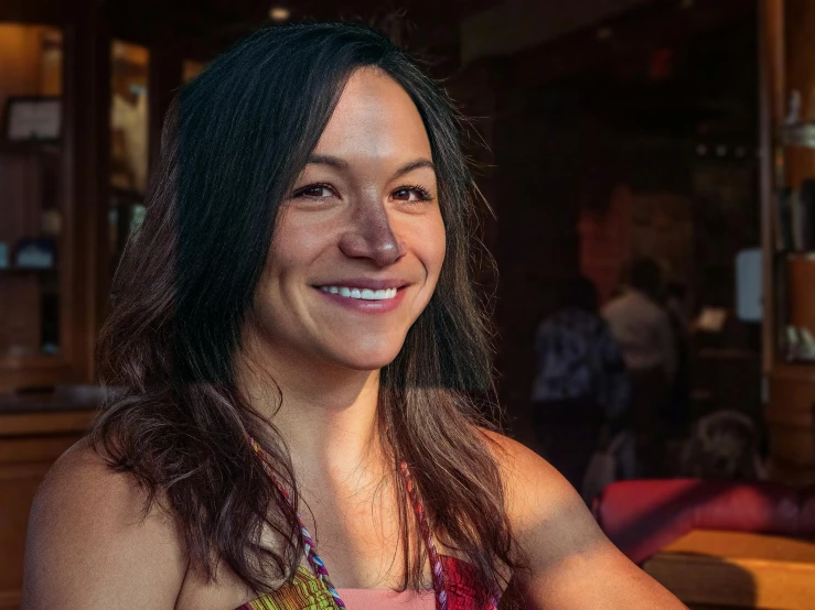 a woman sitting at a table with a plate of food, portrait of danny gonzalez, profile image, happily smiling at the camera, dim lit