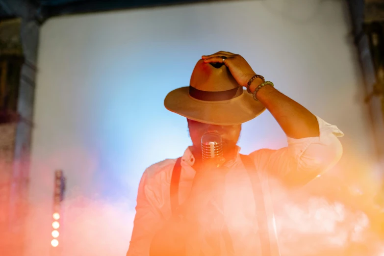 a man wearing a hat standing in front of a stage, pexels, flare, thumbnail, high quality image, brown