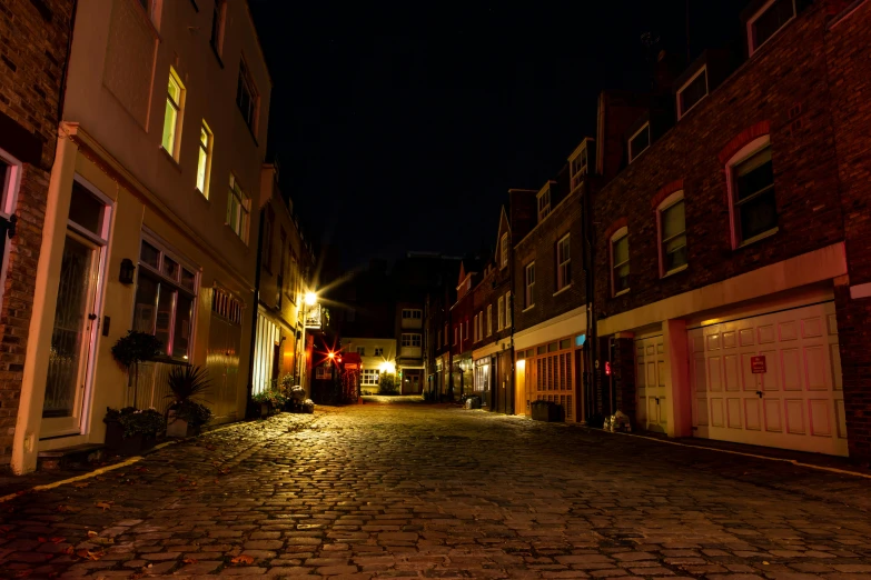 a cobblestone street is lit up at night, by IAN SPRIGGS, unsplash, victorian harbour night, deserted, night time footage