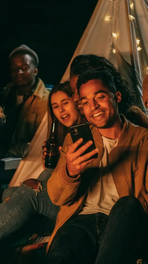 a group of friends sitting around a campfire taking a selfie, trending on pexels, happening, brown skin man with a giant grin, tv commercial, holding a drink, [ theatrical ]