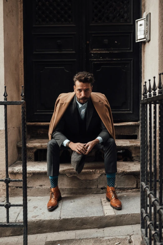 a man sitting on the steps of a building, a portrait, inspired by Harrington Mann, pexels contest winner, renaissance, trench coat and suit, short brown beard, humans of new york style, about to step on you