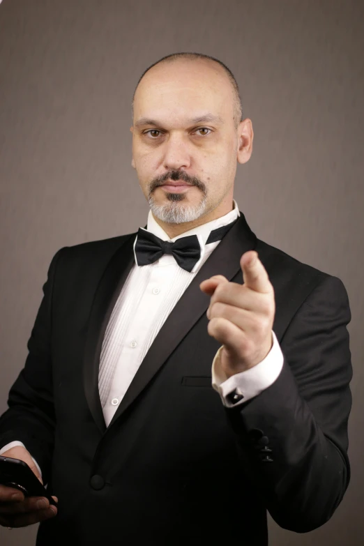 a man in a tuxedo holding a cell phone, an album cover, inspired by Edi Rama, pointing index finger, adar darnov, professional photo-n 3, bald