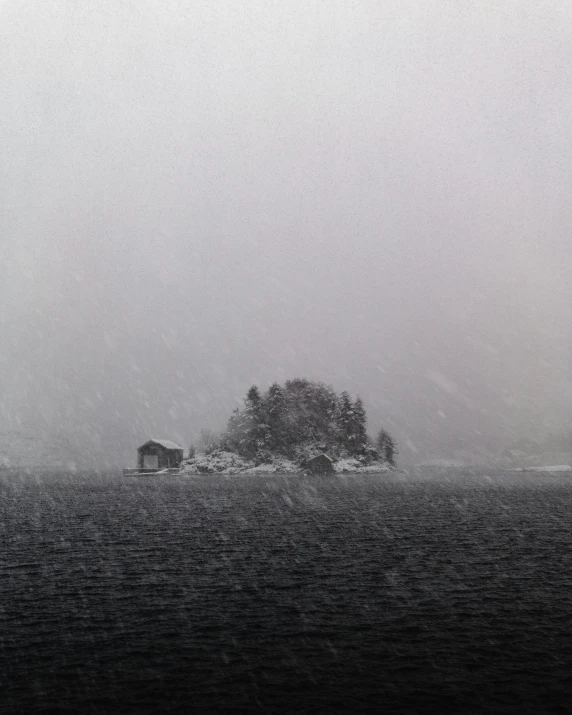 a black and white photo of a small house in the middle of a lake, by Roar Kjernstad, snow flurries, an island, in muted colours, ( ( photograph ) )