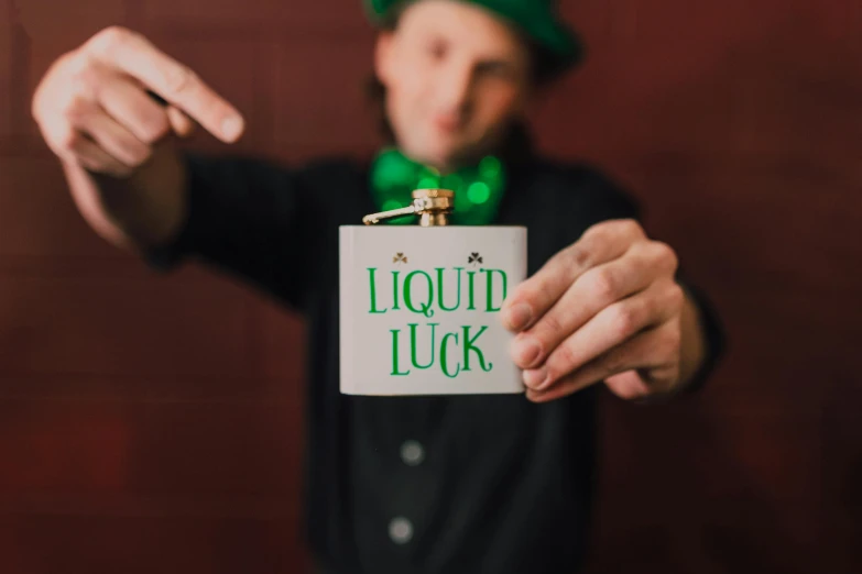a man in a green hat holding a sign, by Nicolette Macnamara, pexels contest winner, liquids, magic item, four leaf clover, holding a drink