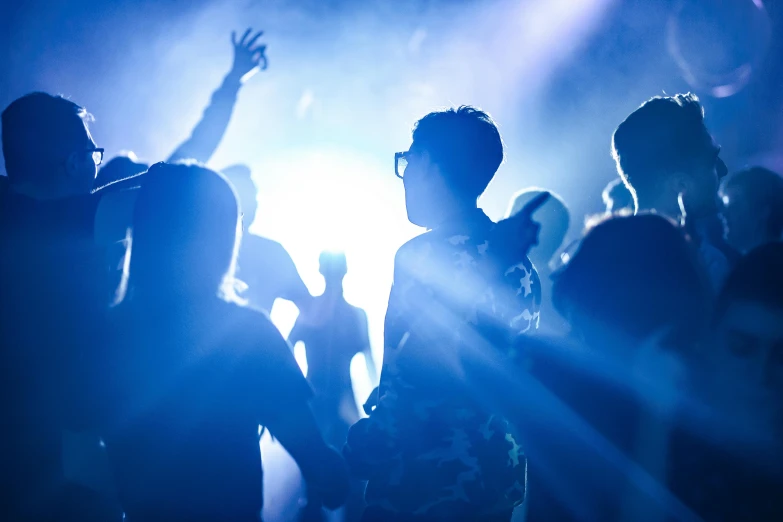 a group of people standing next to each other at a concert, by Lee Loughridge, pexels, happening, bursting with blue light, photograph of three ravers, silhouetted, jesus wasted at a party