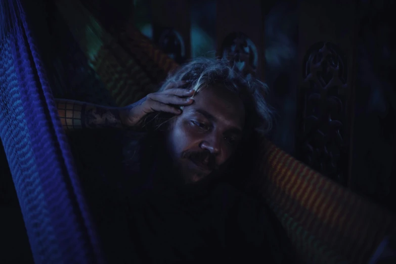 a man laying in a hammock in the dark, inspired by Elsa Bleda, pexels contest winner, portrait of crazy post malone, concerned, standing in a dimly lit room, ayahuasca ceremony