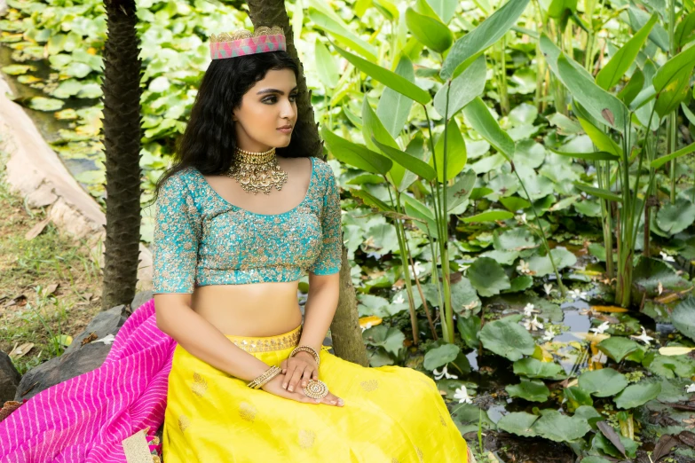 a woman sitting on a rock in a yellow skirt, trending on cg society, hurufiyya, blue colored traditional wear, curated collections, intricate silk clothing, promotional image