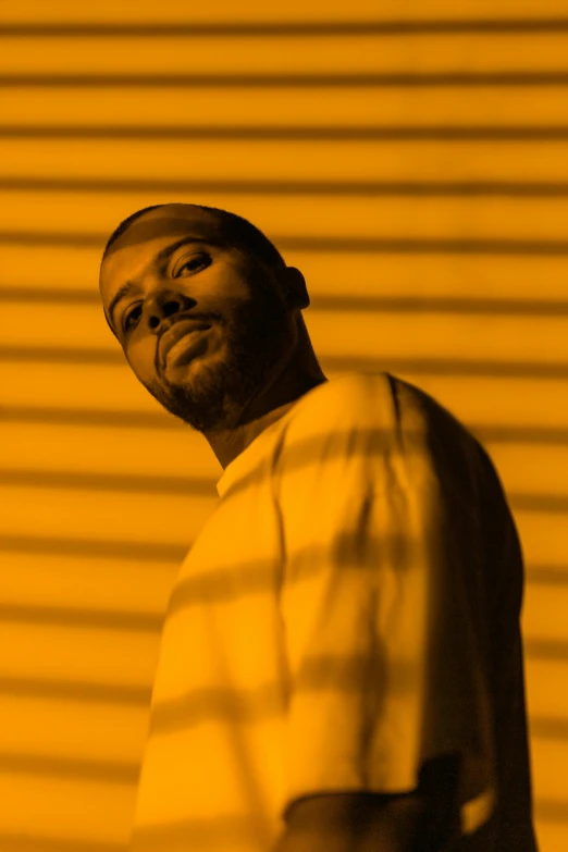 a man standing in front of a yellow wall, an album cover, inspired by Paul Georges, frank ocean, standing in a dimly lit room, portrait photo of a backdrop, scrolls