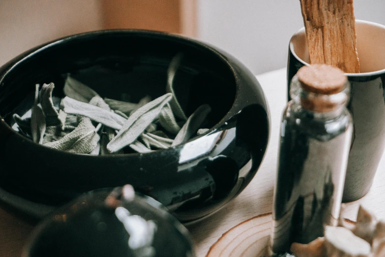 a black bowl sitting on top of a wooden table, a still life, trending on pexels, lots of jars and boxes of herbs, sage ( valorant ), candy treatments, wearing a grey robe