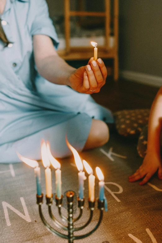 a woman sitting on the floor holding a lit candle, by Julia Pishtar, pexels contest winner, children playing with pogs, happy birthday candles, blue tunic and robes, on a candle holder