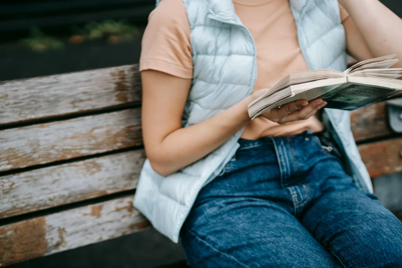 a woman sitting on a bench reading a book, trending on pexels, cropped shirt with jacket, denim, holding a book, 1450