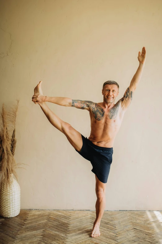 a man standing in the middle of a yoga pose, a photo, arabesque, lean man with light tan skin, shows a leg, davey baker, 4 5 yo