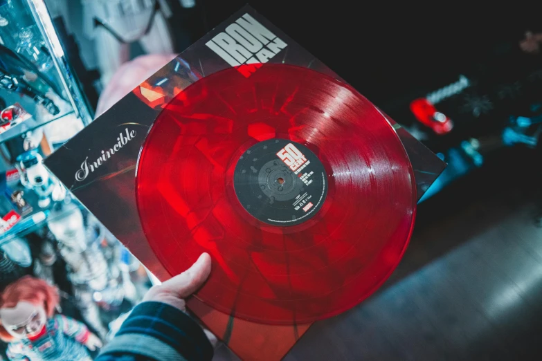 a person holding up a red vinyl record, an album cover, by Romain brook, unsplash, in plastic, metallic red, carnage, ironman