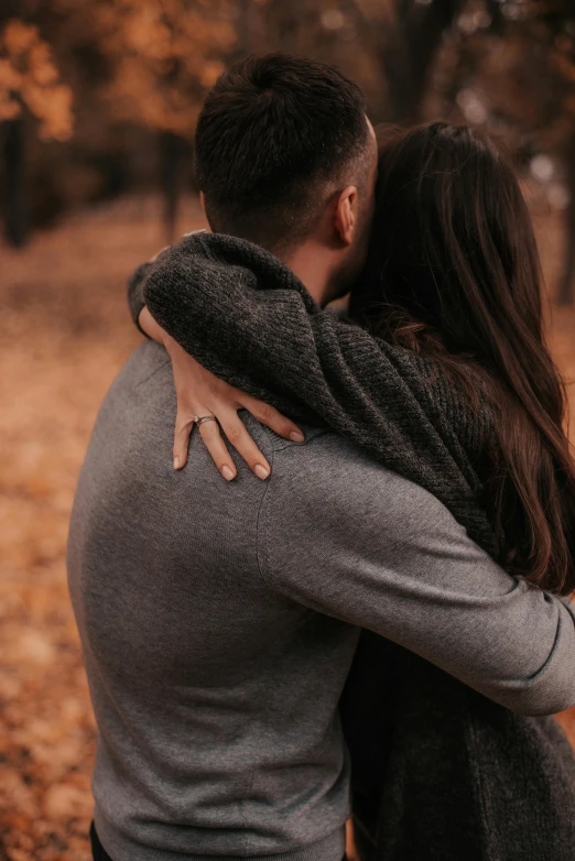 a man and woman hugging each other in a park, trending on pexels, he is wearing a brown sweater, back, tight, romantic lead