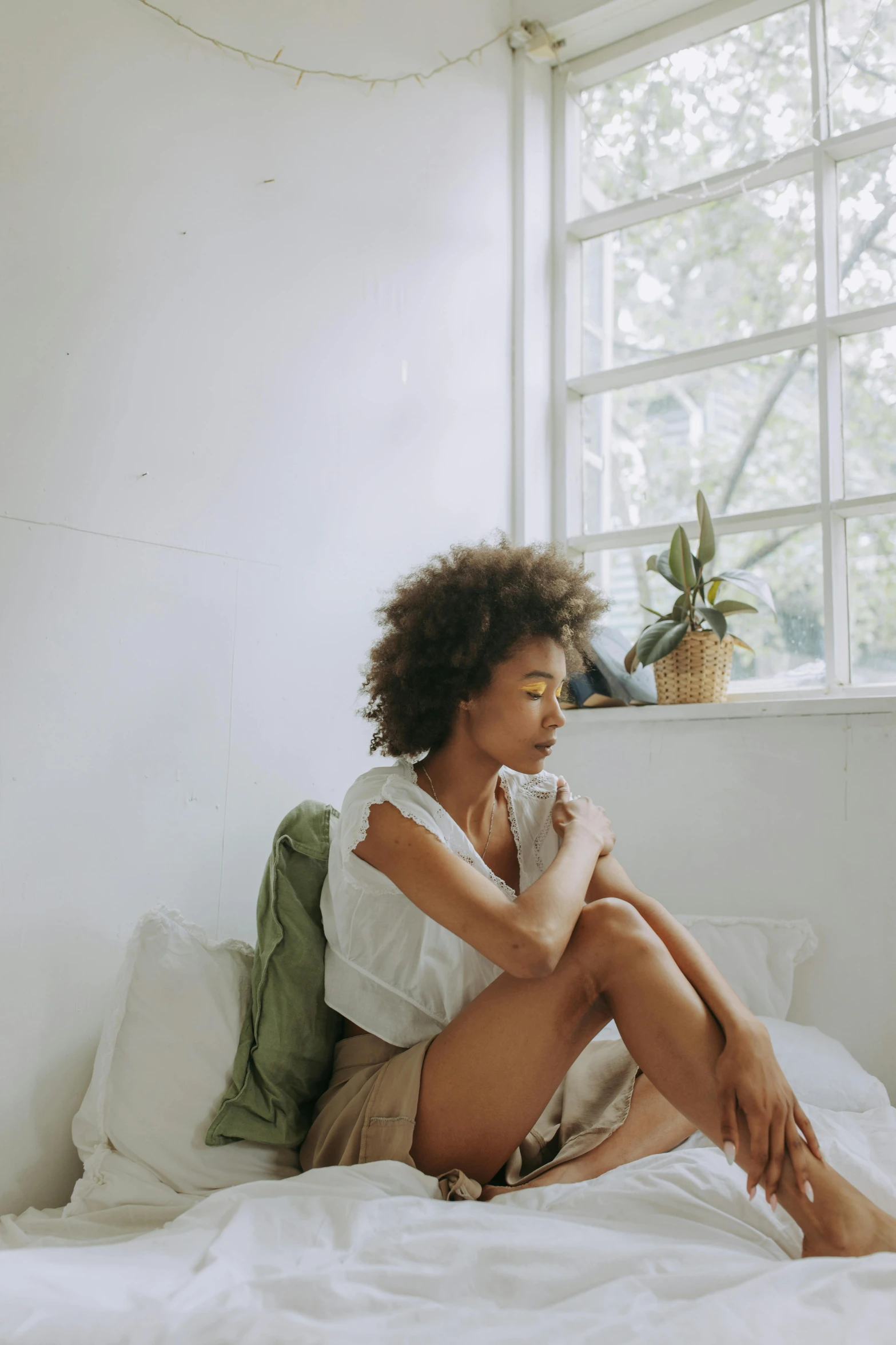 a woman sitting on top of a bed next to a window, by Dulah Marie Evans, trending on pexels, visual art, curls on top, soft green natural light, ashteroth, concerned