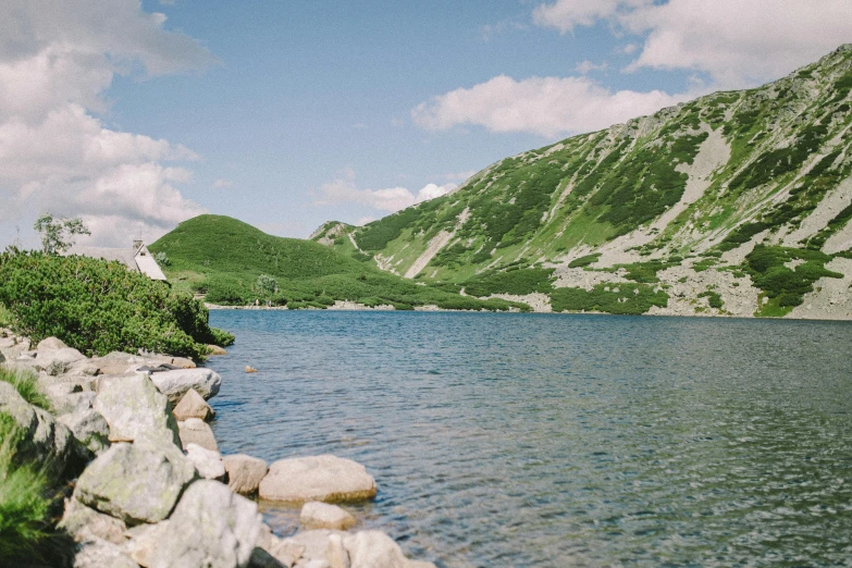 a large body of water sitting on top of a lush green hillside, by Emma Andijewska, pexels contest winner, sōsaku hanga, a photo of a lake on a sunny day, 1990's photo, rocky lake shore, conde nast traveler photo