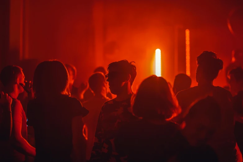 a group of people standing in front of a red light, underground party, profile image, orange hue, hazy