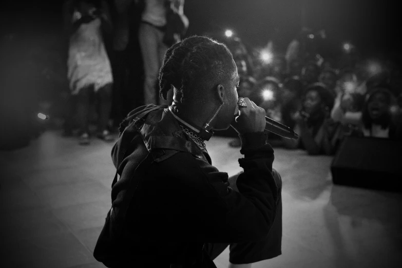 a man singing into a microphone in front of a crowd, an album cover, pexels, visual art, xxxtentacion, monochrome, facing away from the camera, chief keef