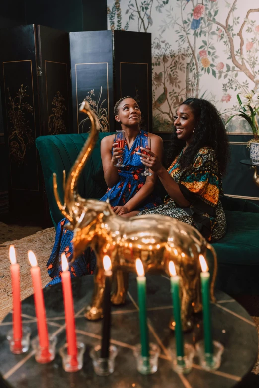 two women sitting on a couch with candles in front of them, trending on unsplash, black arts movement, wearing festive clothing, in their noble mansion, wearing an african dress, cheers