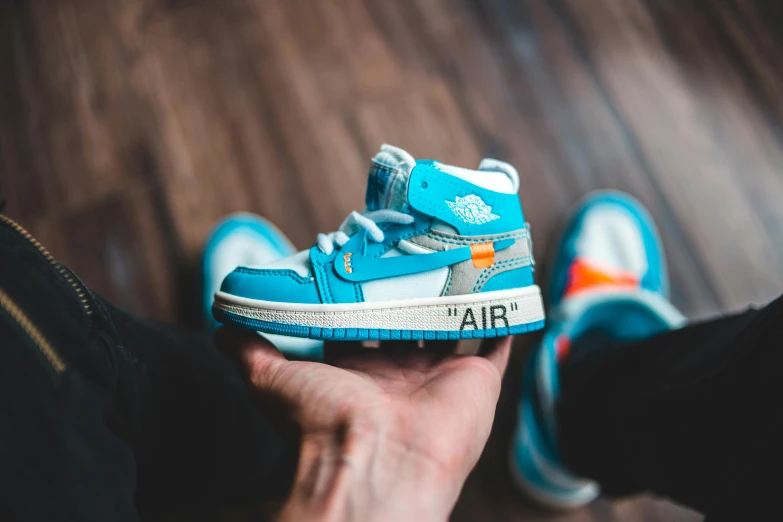 a person holding a pair of shoes in their hand, a cartoon, unsplash, “air jordan 1, orange and cyan paint decals, toy photo, uniform off - white sky