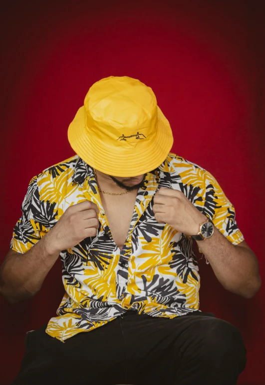 a man in a yellow hat sitting on a chair, an album cover, pexels, hurufiyya, summer shirt, patterned, palms, saturation 40