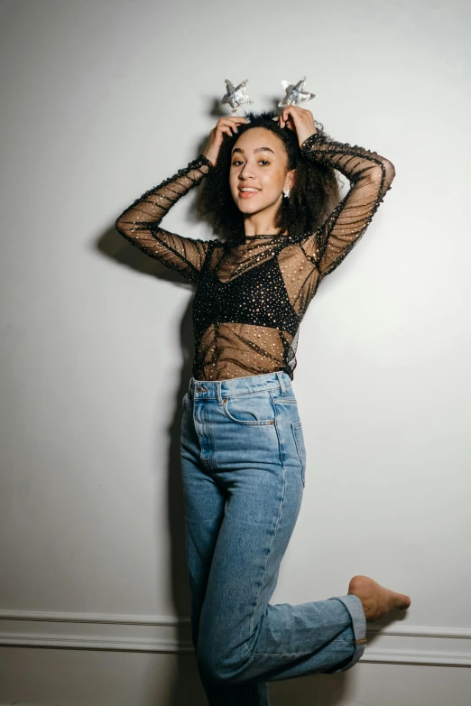 a woman posing in front of a white wall, by Robbie Trevino, mesh shirt, ashteroth, ( ( ( wearing jeans ) ) ), young woman in her 20s